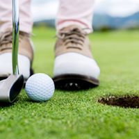 Close up of feet of golfer, golf club and ball beside hole